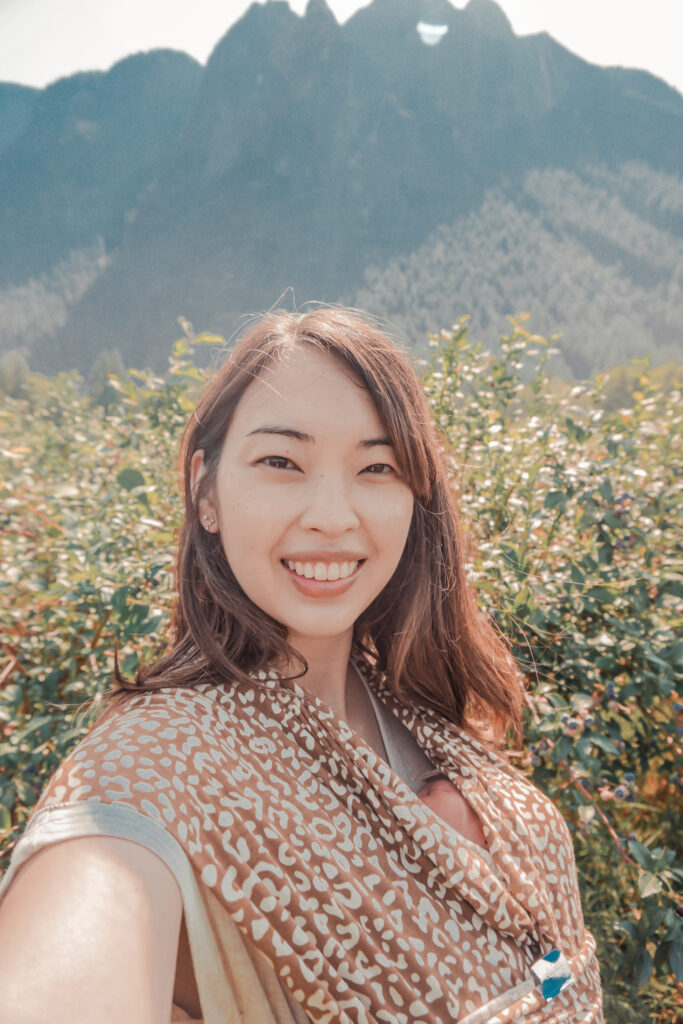 Mom taking a selfie with a newborn in a leopard print Solly Baby Wrap, mountain in the background