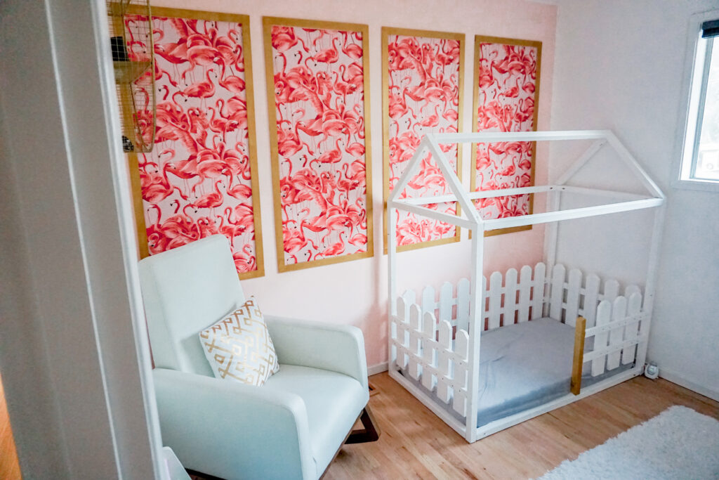 girls nursery room: flamingo wallpaper with gold frame in modern chinoiserie on a pink wall, white modern rocking chair, and white wooden house bed