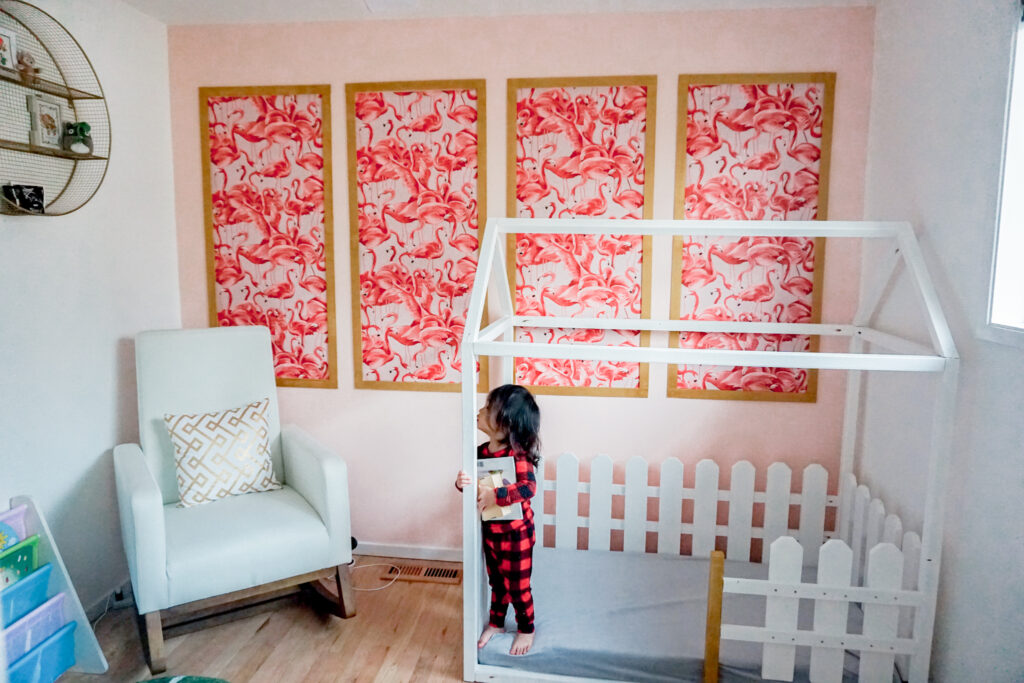 girls nursery room: flamingo wallpaper with gold frame in modern chinoiserie on a pink wall, white modern rocking chair, and white wooden house bed