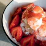 closeup of korean shaved ice (bingsu) in a bowl with sliced strawberries and strawberry syrup