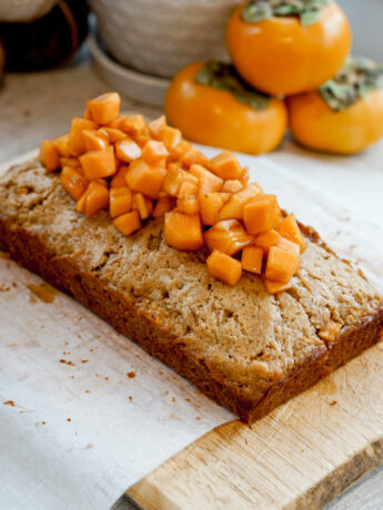 angled overhead shot of persimmon cake with chopped persimmons on top and stack of persimmons in the background