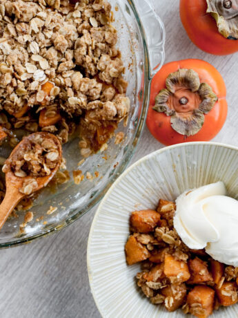 overhead shot of persimmon crisp in glass baking dish with a serving scooped out into a ceramic bowl with vanilla ice cream