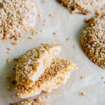 angled shot of tahini cookies on a baking tray with one cut in half