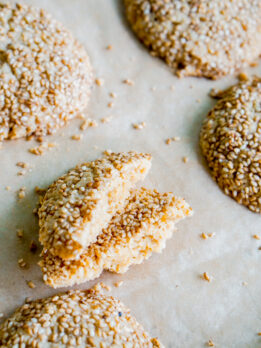 angled shot of tahini cookies on a baking tray with one cut in half