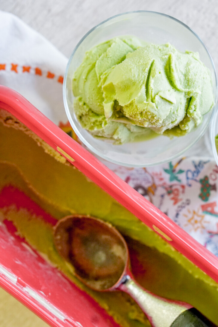 matcha ice cream in small clear bowl next to 1.5 qt ice cream container with scoop inside