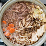 overhead shot of sukiyaki in a clay pot over stovetop