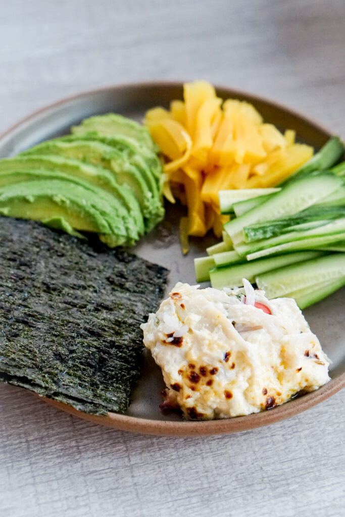 Plate of broiled sushi bake, cucumber, pickled daikon, avocado, and seaweed.