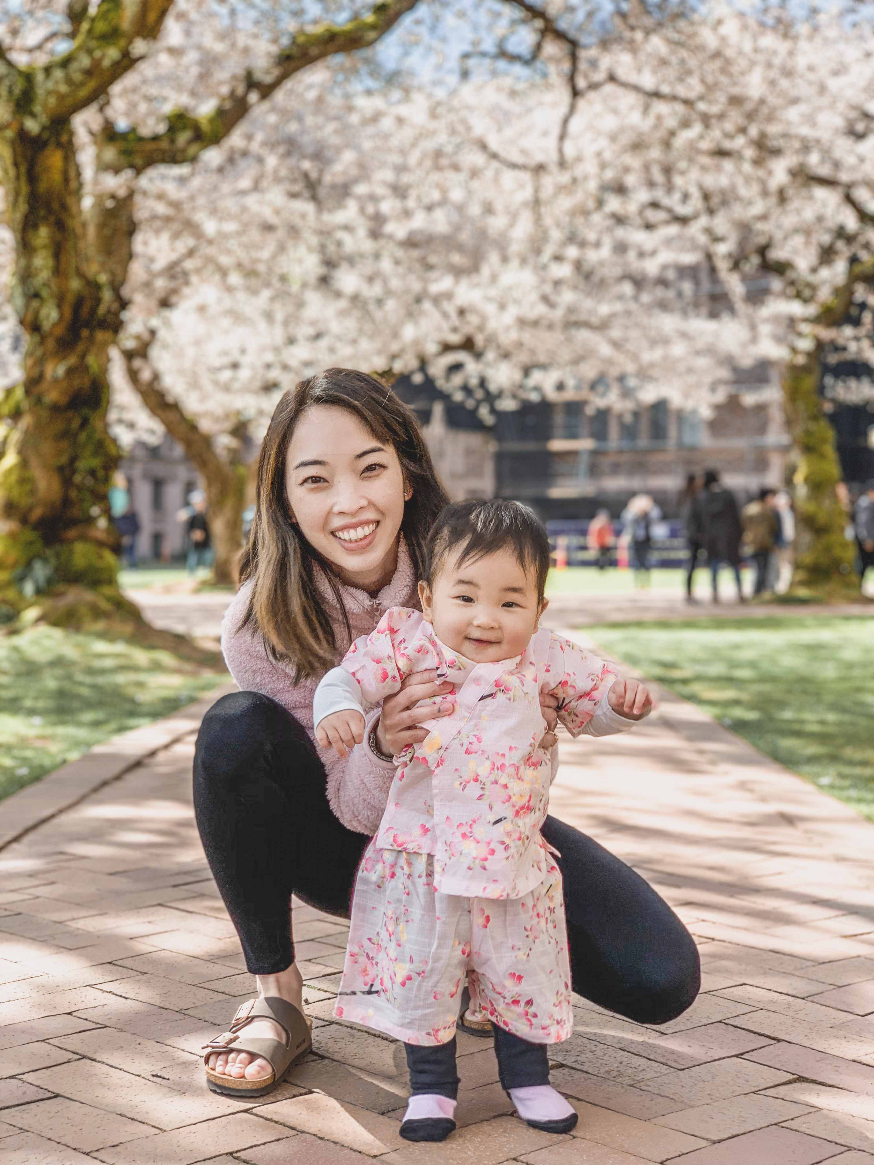 Asian mom with baby girl wearing pink kimono looking at the cherry blossoms at University of Washington