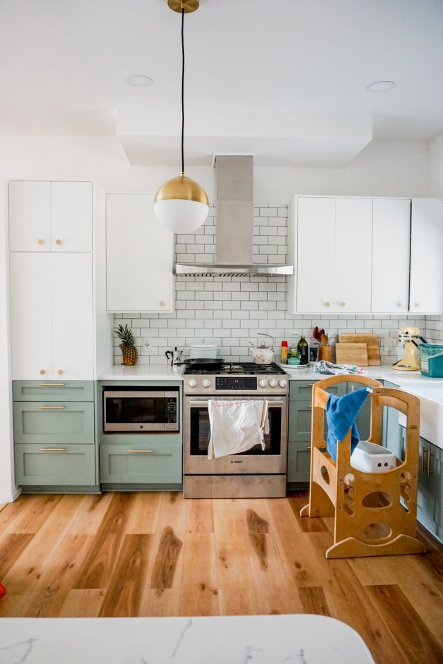 mid century modern kitchen renovation - two toned white and green cabinets, marble countertops, globe pendant light, gold hexagon knobs, and gold cabinet pulls