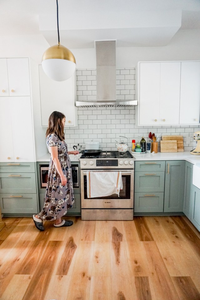 mid century modern kitchen renovation - two toned white and green cabinets, marble countertops, globe pendant light, gold hexagon knobs, and gold cabinet pulls
