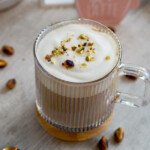 pistachio latte in clear mug with milk foam and chopped pistachios on top